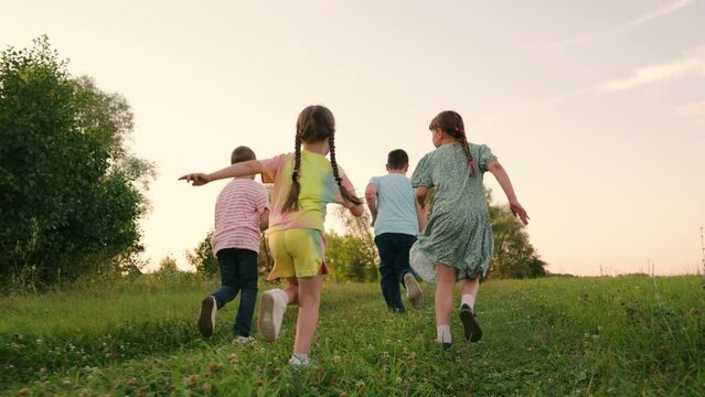 Children play in park, friends run on green grass. Concept of happy childhood dream. Happy boy and girl running, playing together in nature. Family, weekend outdoors. Kids running, healthy lifestyle