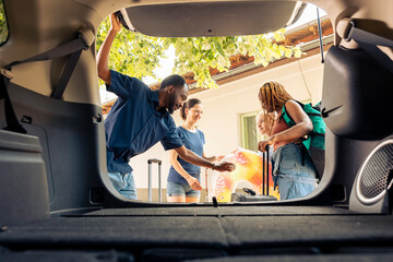 Multiethnic people loading baggage in trunk, preparing car with trolley and travel bags to leave on holiday trip. Travelling together on vacation adventure during summer, seaside journey.
