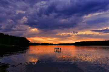 Orange summer sunset with violet clouds on the lake