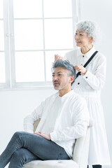 Obraz premium 美容院で働く美容師とヘアセットされるシニア男性（美容・仕事）