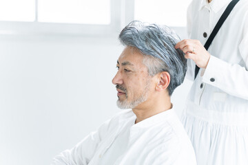 美容院で働く美容師とヘアセットされるシニア男性（美容・仕事）