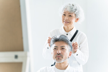 美容院で働く美容師とヘアセットされるシニア男性（美容・仕事）