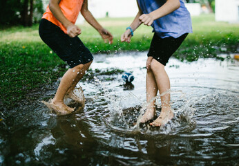 Two children jump into a rain puddle in green field