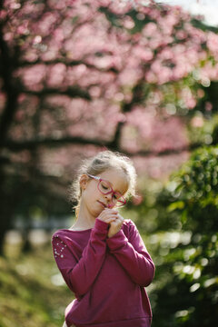 Blond haired girl child smells flower in front of sakura blossoms