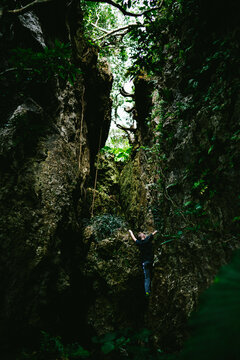 Boy hikes and climbs up a cliff in a tropical forest