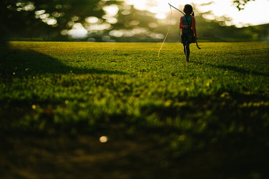 Girl child walks through green grass field in golden light