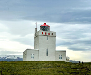 Fototapeta na wymiar Vik, Iceland - July 3, 2022 View of the Dyrhólaey Lighthouse, a square concrete tower, painted white with red trim, located on the central south coast of Iceland.