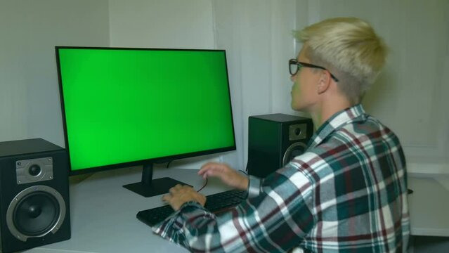 Guy is typing text on the keyboard then turns around and does strange smile. Chromakey on computer screen. Video with a chroma key on the screen to insert any video.