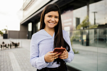 Young businesswoman using smartphone in downtown streets near business buildings