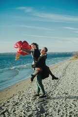 Happy running couple with a red heart balloons on the beach
