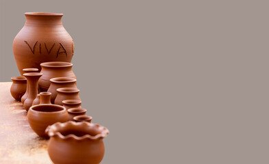 Fototapeta na wymiar Master class on modeling on a pottery wheel. A few example of raw ceramic jars, vases and pots out of clay. The sign 'Viva' or 'Long life