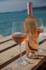 Glasses and bottle of cold rose wine from Provence served outdoor on wooden yacht pier with view on blue water and white sandy beach Plage de Pampelonne near Saint-Tropez, France