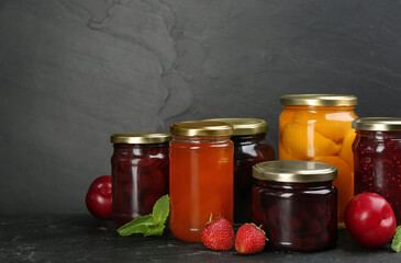 Jars of pickled fruits and jams on grey table