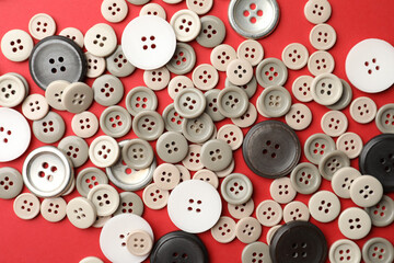 Many colorful sewing buttons on red background, flat lay