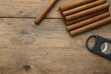 Cigars and guillotine cutter on wooden table, flat lay. Space for text