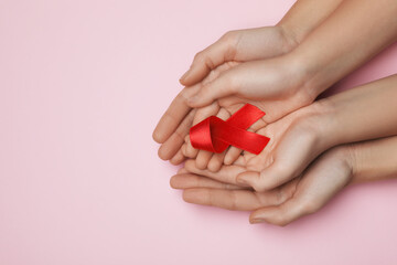 Woman and girl holding red ribbon on pink background, top view with space for text. AIDS disease awareness