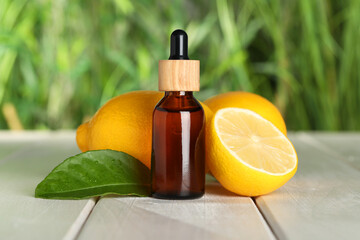 Bottle of essential oil with lemons and leaf on white wooden table against blurred background,...