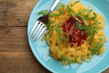 Tasty spaghetti squash with tomato sauce and arugula served on wooden table, top view