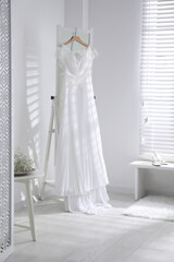 Beautiful wedding dress hanging on mirror in room