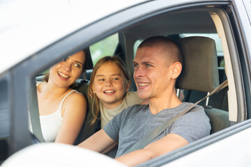 Positive young adult man driving car during trip with his family, woman and little girl