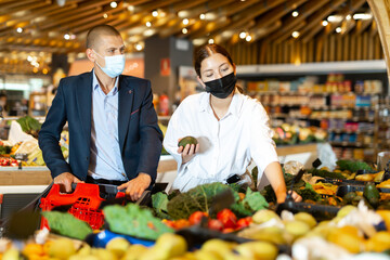 Portrait of young woman and man in face mask for disease protection doing shopping at vegetables...