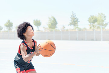 African-American boy ready to shoot the ball while plays in a basketball game on a court at a sports facility. Healthy life concept.