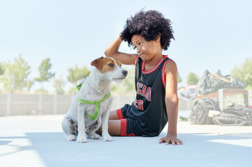 African-American kid with his small dog, resting after playing a basketball game on a court at a sports facility. Sportive life concept.