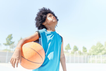 African-American boy focused on the basket and holding the ball is ready to play in a basketball game on a court at a sports facility. Sportive life concept.