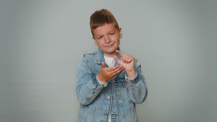 Need some more please give me. Boy showing a little bit gesture with sceptic smile, showing minimum sign, measuring small size, asking for help. Children teenager child kid on gray studio background