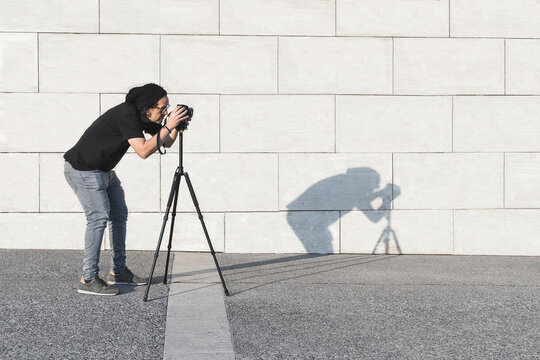 Caucasian male photographer taking photos with tripod in the daytime with grey background wall and copy space  .