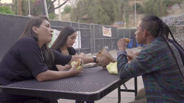 Native American students and teacher engage in a conversation over lunch on a school bench.