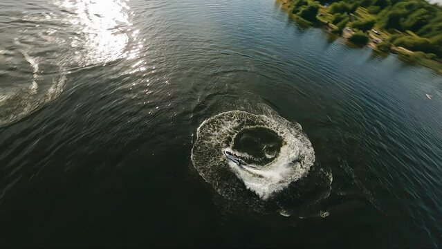 A guy on a jet ski rides on the surface of the lake writing out cool tricks. There are traces on the water