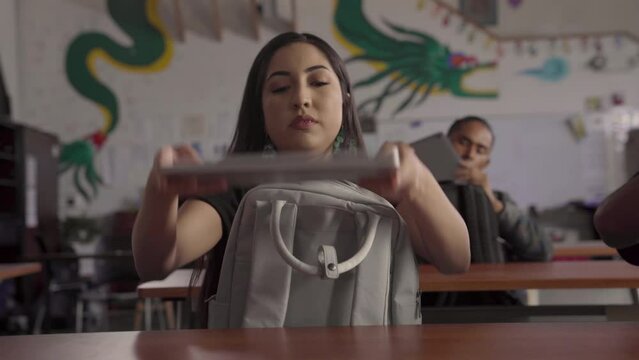 Native American girl takes her school supplies out of her bag and sets them on the table.