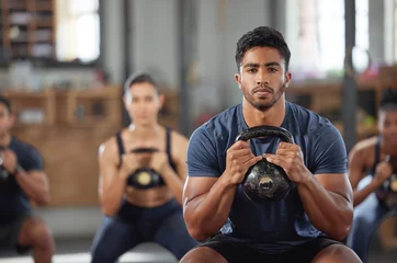  Personal trainer squatting with a team of athletes in a workout session at a fitness club. Portrait of a fit, active and serious young male coach using a kettlebell and training a group of people © Alexis Scholtz/peopleimages.com