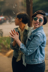 Pretty and cheerful young generation z girl with short hair dressed in blue with a denim jacket, sunglasses and gold jewelry posing in front of a reflective surface with a slight gold color.
