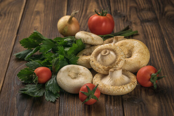 Fresh milk mushrooms, tomatoes and a bunch of parsley on a wooden background.