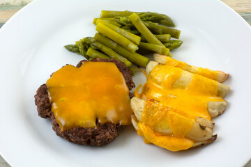 Warm meal of hamburger patty and potato wedges with melted cheddar cheese and asparagus on white plate
