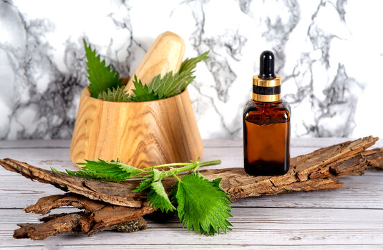 Fresh nettle in a wooden mortar. Preparation of elixirs from medicinal herbs by herbalists. The essential oil in the pharmacy bottle with pipette at cosmetologi