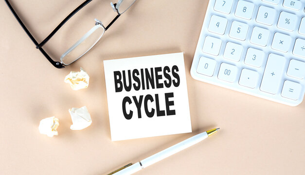 BUSINESS CYCLE text on sticky with pen ,calculator and glasses on a beige background