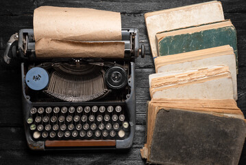 Fototapeta na wymiar Retro style typewriter and stack of books on the black wooden flat lay background.