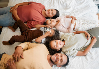 Fun family, children and parents bonding while lying on a bed in home bedroom from above. Portrait of playful, smiling and happy kids having fun with mother and father on weekend and making memories