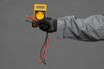 Electrician hand with the multimeter tool on the gray background.