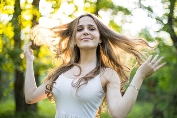 Beautiful young Russian girl dressed in a white dress, walks through the forest among the oaks in the rays of the sunset