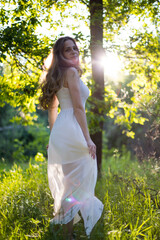 Beautiful young Russian girl dressed in a white dress, walks through the forest among the oaks in the rays of the sunset