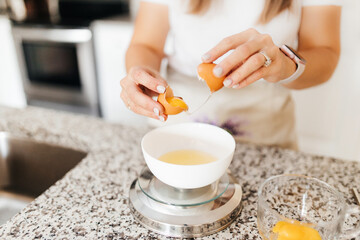 A young beautiful woman cooks in a bright kitchen, hands and broken eggs closeup. A cute girl separates the whites from the yolks for baking cakes. Cooking macaroons.