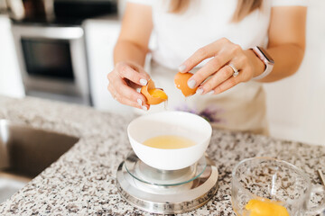 A young beautiful woman cooks in a bright kitchen, hands and broken eggs closeup. A cute girl separates the whites from the yolks for baking cakes. Cooking macaroons.