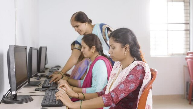 Trainer guiding studnets while teaching computer class to woman's at village - concept of self employment training and empowerment programs.
