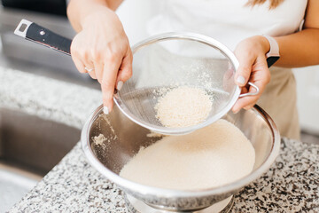 A young beautiful woman cooks in a bright kitchen. Cooking macaroons. A cute girlp repares dough for cakes, hands and ingrident closeup. Cooking macaroons. Cookie baking