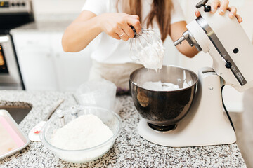 Fototapeta na wymiar A young beautiful woman cooks in a bright kitchen. Cooking macaroons. A cute girlp repares dough for cakes, hands and ingrident closeup. Cooking macaroons. Cookie baking