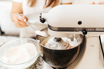A young beautiful woman cooks in a bright kitchen. Cooking macaroons. A cute girlp repares dough for cakes, hands and ingrident closeup. Cooking macaroons. Cookie baking